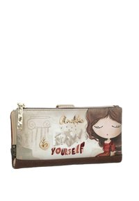 Cartera con la imagen de una niña con los ojos cerrados, cremallera decorativa, charm en forma de corazón, texto en relieve "Disfrútate" e ilustración de una columna cosida sobre fondo beige.