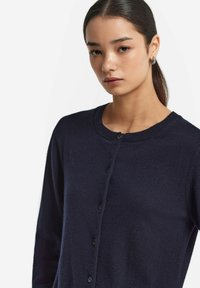 Granatowy, dzianinowy kardigan z okrągłym dekoltem, z zapięciem na guziki i teksturowanym materiałem. Gładkie wykończenie i standardowy krój.