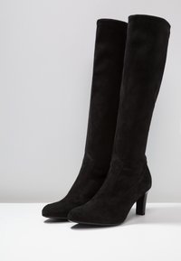 Bottes montantes en daim noir avec un bout effilé et un talon empilé, présentant une texture lisse et une construction sans coutures.