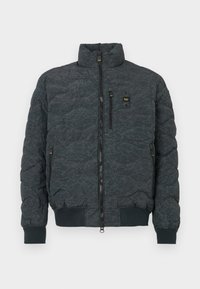Jachetă puffer matlasată de culoare gri închis, cu guler înalt, fermoar frontal, două buzunare laterale și manșete elastice. Prezintă o textură subtilă și un accent cu logo.