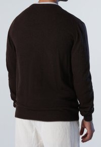 Pull marron foncé en tissu doux avec un col rond, des poignets et un ourlet côtelés, présenté de dos, assorti à un pantalon en velours côtelé blanc.