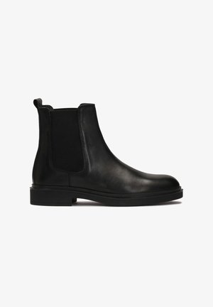 Bottes Chelsea en cuir noir avec panneaux élastiques sur les côtés, bout rond, texture lisse et talon bas. Design minimaliste.