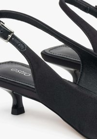 Czarne sandały na obcasie wykonane z miękkiego materiału, z wąskim obcasem, regulowanym paskiem z klamrą i logo na wkładce.