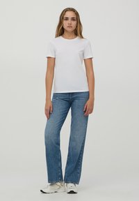 T-shirt bianca in cotone con maniche corte, abbinata a jeans dritti azzurri e scarpe da ginnastica bianche. Design semplice e informale.