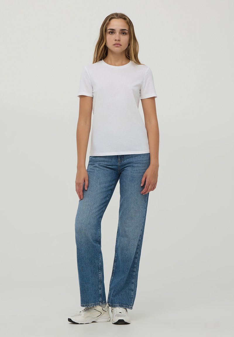 T-shirt bianca in cotone con maniche corte, abbinata a jeans dritti azzurri e scarpe da ginnastica bianche. Design semplice e informale.
