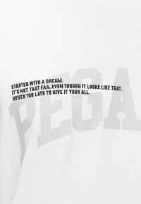 Biały materiał z dużymi wyblakłymi literami i mniejszym czarnym tekstem brzmiącym: "Zaczęło się od marzenia. To nie jest tak daleko, mimo że tak to wygląda. Nigdy nie jest za późno, aby dać z siebie wszystko."