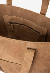 Interieur van een bruine suède totebag met een ritszak met een gladde textuur. Open ontwerp met versterkte handvatten voor duurzaamheid.