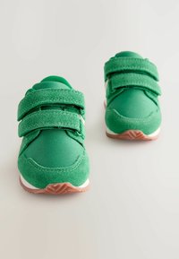 Zielone trampki wykonane z teksturowanej tkaniny, z dwiema rzepami, wyposażone w gumową podeszwę oraz wzmocniony czubek, co zapewnia trwałość i przyczepność.