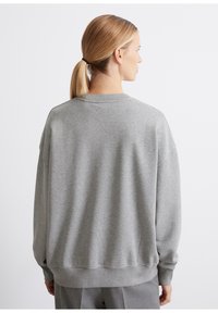 Šedá mikina s voľným strihom, okrúhlym výstrihom a rebrovanými manžetami. Vyrobená z mäkkého materiálu, s hladkou textúrou a minimálnym dizajnom.