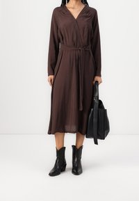 Brun, långärmad, omlottklänning med ett knyt i midjan. Matchad med svarta, ankellånga stövlar och en svart läderhandväska. Slät textur.