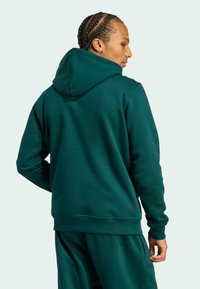 Tmavo zelená mikina s veľkou kapucňou, mäkký materiál, ribované manžety a voľný strih, v kombinácii s ladícími teplákmi.