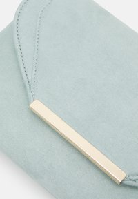 Clutch de ante azul claro con un acento rectangular en tono dorado. Presenta una textura suave y detalles de costura que crean un diseño elegante.