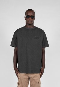 Graues Baumwoll-T-Shirt mit Rundhalsausschnitt, kurzen Ärmeln und einem dezenten Logo-Detail in Weiß auf der linken Brust. Angenehme Textur.