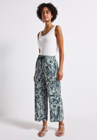 Wide-leg pants in a blue and white snake print, made of lightweight fabric with an elastic waistband and drawstring. Paired with a fitted white tank top.