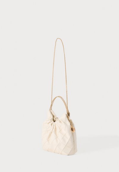 Sac à main matelassé de couleur crème avec une bandoulière en chaîne dorée et un petit cadenas doré sur un fond uni.