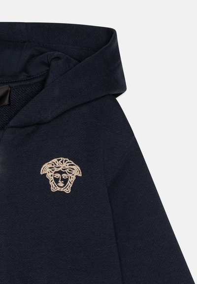Sudadera navy con un tejido texturizado, que presenta un diseño bordado en crema de una cara en la parte izquierda del pecho.