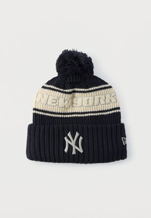 Temno modra pletena kapa s kremno črto in napisom "NEW YORK". Ima cof na vrhu in rebrast manšetni del. Prikazana z logotipom Yankees.