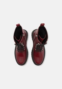 Botine roșii din piele cu un finisaj neted, talpă din cauciuc negru în contrast și detalii metalice la șireturi pentru o fixare sigură.