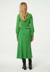 Grüner ribbeliger Strickpullover und dazu passender langer Rock, beide aus weichem Material, kombiniert mit schwarzen, knielangen Stiefeln mit Nietenakzenten.