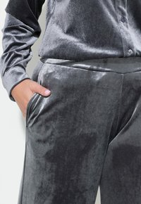 Samtgraues Loungewear-Set mit einem Knopfverschluss-Oberteil und lockeren Hosen mit Seitentaschen. Glatte Textur und elegantes Design.