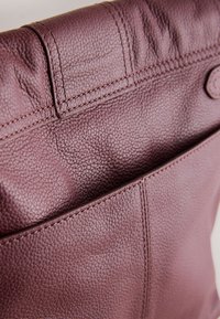 Leren handtas in diep bordeauxrood met een korrelige textuur, voorzien van zichtbare stiksels en een detail van een voorvak.