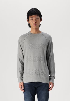 Heled hall pikka varrukaga kampsun tekstuuriga mustriga, millel on horisontaalsed triibud ja ümmargune kaelus. Koos tumedate teksadega.