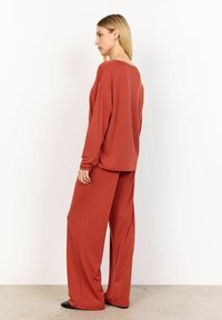 Maglietta a maniche lunghe in rust e pantaloni a gamba larga realizzati in tessuto morbido. L'insieme presenta una vestibilità comoda con scollatura rotonda e cuciture minime.