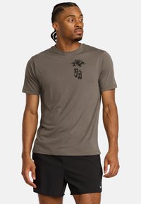T-shirt verde oliva a maniche corte in un materiale morbido e traspirante, con grafiche di rose nere e testo sul petto, abbinato a pantaloni corti neri.