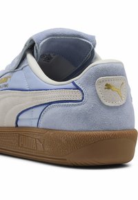 Svetlo modra tenisa z nobukom in sintetičnim materialom, rjav gumijast podplat, oblazinjena zgornja obreza ter zlat logo Puma na peti in strani.