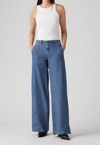 Vidbenade blå denimjeans med hög midja, med framfickor och knappstängning. Parat med en tight vit linne.