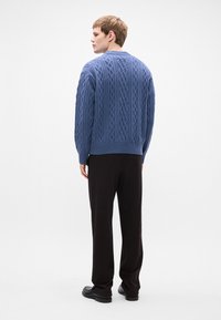 Blauwe gebreide trui met een kabelpatroon, ronde hals en geribbelde zoom, gecombineerd met zwarte, losse broek en zwarte schoenen.