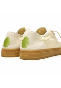 Zapatillas de lona beige con un emblema de árbol verde en la parte trasera, con un tejido texturizado, suela de goma y detalles de costura en contraste.