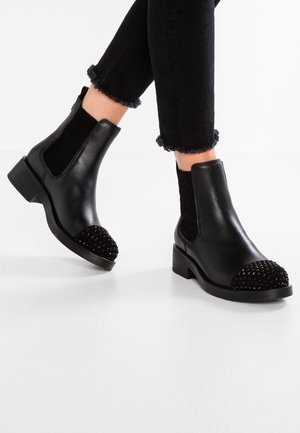 Bottines en cuir noir avec un bout arrondi orné de perles noires. Panneaux latéraux élastiques et un petit talon carré. Détail de chaussette en tissu texturé.