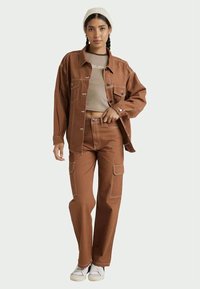 Brown denim jacket with white stitching, paired with matching cargo pants. Light beige cropped top underneath, complemented by white sneakers.