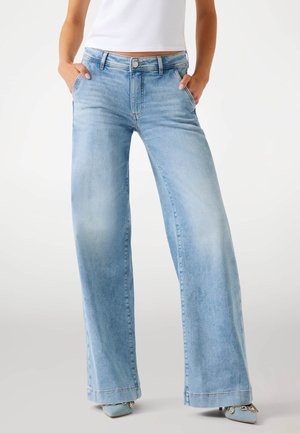 Jean large bleu clair en denim, avec taille haute, design à cinq poches, et une finition délavée avec des détails de whiskering subtils.