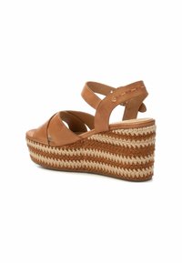Sandali con zeppa in pelle marrone con suola in paglia intrecciata. Presentano cinturini incrociati e un design testurizzato sulla zeppa.