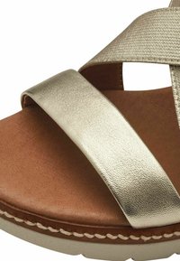 Goldfarbene, metallische Sandale mit einem breiten, glatten Riemen, beigefarbenem Lederfußbett und strukturiertem Profil. Beachten Sie die kontrastierenden Nähte.