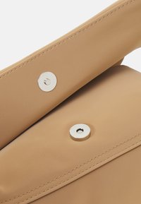 Brun handväska i slätt, strukturerat material, med silverfärgade tryckknappar och prydlig söm längs kanterna. Kompakt och minimalistisk design.