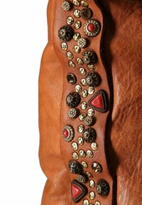 Cuoio tan con decorazioni, tra cui pietre rosse e borchie metalliche di varie forme e dimensioni, che evidenziano dettagli intricati.