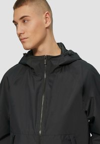 Zwarte capuchonjas met een soepele textuur, voorzien van een volledige rits en een mesh voering. Inclusief verstelbare trekkoorden en schuine zakken.