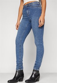 Höga blå denim skinny jeans med en slät yta och subtila blekningar, kombinerade med svarta klackboots.