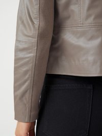 Veste en cuir gris clair au design ajusté, dotée d'accents côtelés le long des manches. Associée à un pantalon en denim foncé.