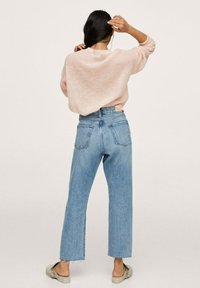 Hellrosa gestrickter Pullover, lockere Passform, kombiniert mit hochtaillierten hellblauen weit geschnittenen Jeans. Praktische Clogs mit elastischen Bändern an den Schuhen.