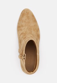 Stivale alla caviglia in suede beige con punta affusolata, dettaglio della cinghia laterale e interno liscio. Superficie testurizzata con un leggero motivo.