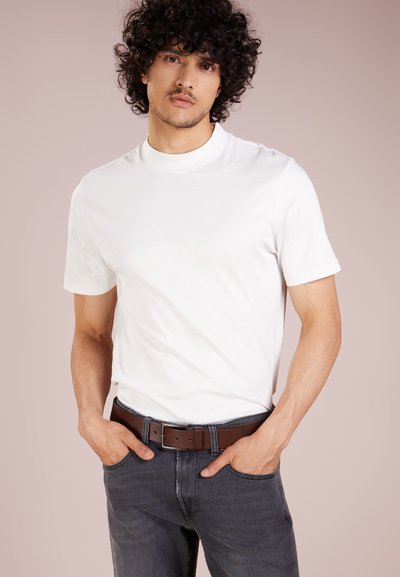 T-shirt en coton blanc à manches courtes, col rond et texture lisse, associé à un jean gris foncé et une ceinture en cuir marron.