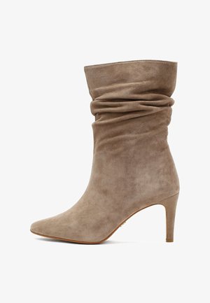 Stivale alla caviglia in suede taupe con design arricciato, punta affusolata e tacco alto sottile. Presenta una texture morbida e dettagli di cuciture sottili.