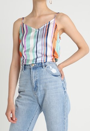 Kvinde iført en ærmeløs, flerfarvet stribet top indstukket i højtailede lyseblå jeans med en slidt lomme detalje.