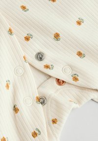 Ribbede cremefarvede bodysuit med spredte orange blomster mønstre. Har sølv- og kobbertrykknapper, blød tekstur og buede kanter.