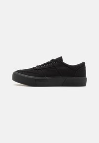 Black canvas sneakers with a textured rubber sole, featuring round laces and a smooth, minimalist design. Accents in matte black.