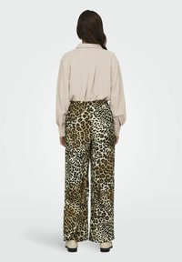 Pantaloni pull-on con stampa leopardata realizzati in un tessuto morbido e testurizzato. Presentano una vestibilità comoda e gambe larghe. Camicia button-up leggermente beige sopra.